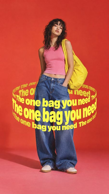 yellow shoulder bag jewelry product photo: A model in a pink tank top and loose blue jeans poses with a bright yellow shoulder bag against a vivid red studio b…