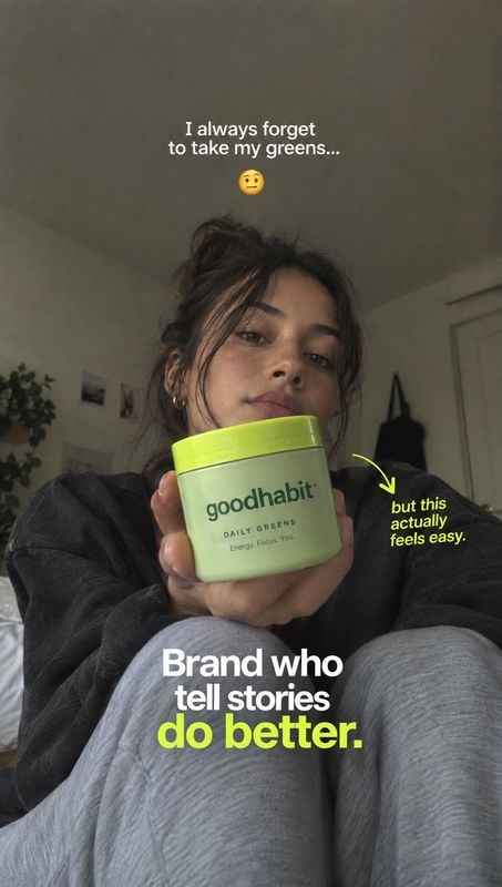 greens supplement powder product in hand product photo: A casually styled woman holds a bright green-lidded greens supplement jar toward the camera in a softly…