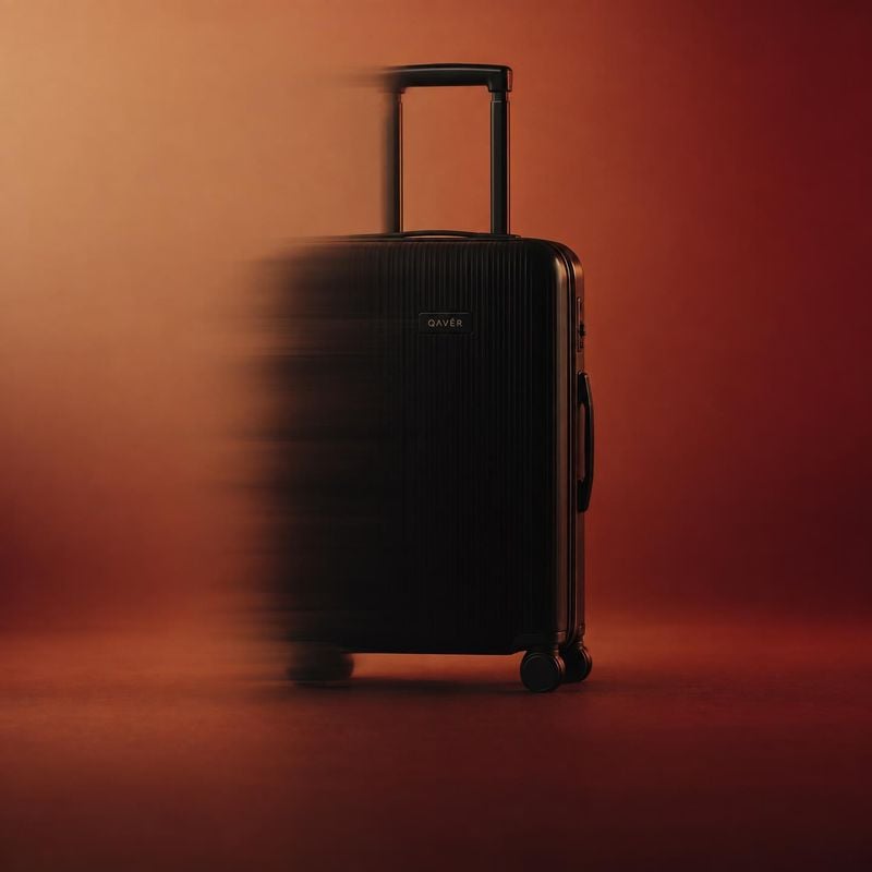 black rolling suitcase action & motion product photo: A black ribbed rolling suitcase stands against a warm red-orange studio backdrop, with motion blur sweepi…