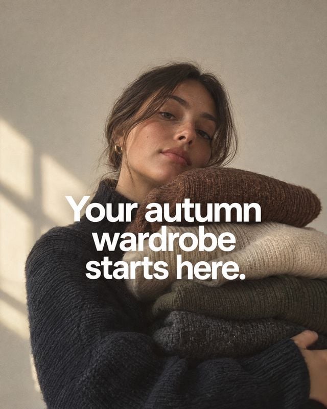 knitwear autumn product photo: A woman in a dark knit sweater holds a stack of cozy autumn knits against a softly sunlit neutral wall, with a bold white wardro…