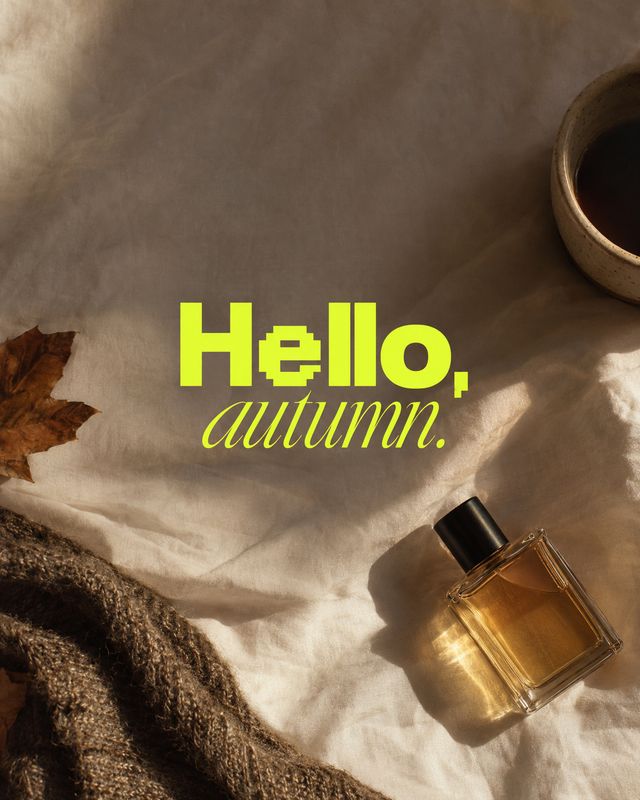 perfume autumn product photo: An amber perfume bottle rests on softly rumpled fabric beside a knit textile, a fallen leaf and a cup, with warm directional ligh…