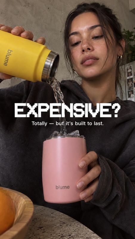 insulated tumbler splash / pour product photo: A woman pours water from a yellow insulated tumbler into a pink one in a softly lit home interior, with bold whi…