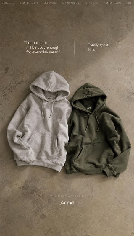 hoodies flat lay product photo: Two neutral-toned hoodies are arranged side by side on a textured concrete surface, with restrained white copy and a muted, und…