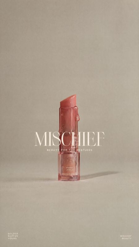 lip balm packshot product photo: A translucent pink lip balm stands alone on a warm beige studio surface, with soft directional light, ample negative space and…