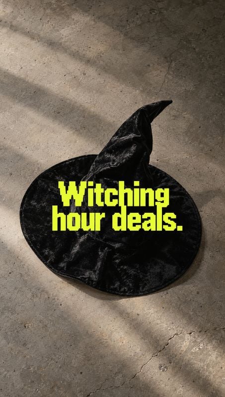witch hat halloween product photo: A black velvet witch hat rests on cracked concrete beneath bold neon-yellow “Witching hour deals” lettering, creating a star…