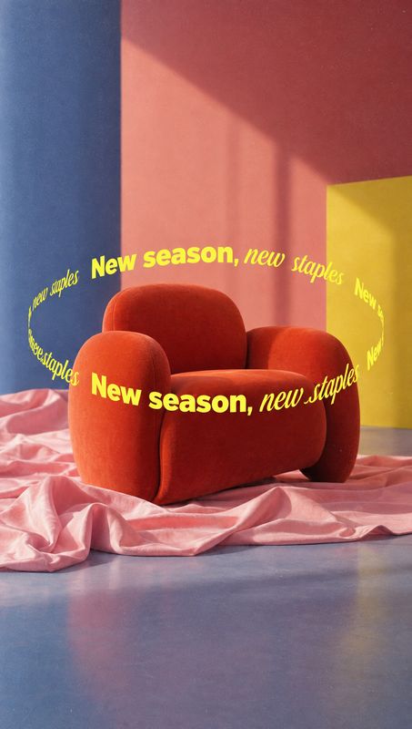 red upholstered armchair room set product photo: A sculptural red armchair sits on rippled pink fabric against bold blue, coral, and yellow studio panels, with…