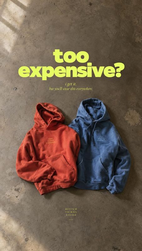hoodies flat lay product photo: Two red and blue hoodies lie side by side on a textured concrete floor, lit by soft angled daylight beneath a bold lime headlin…