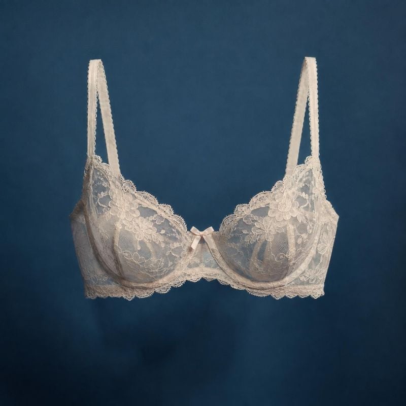lace bra floating product product photo: A delicate ivory lace bra floats against a deep blue studio backdrop, with soft directional lighting giving the image…