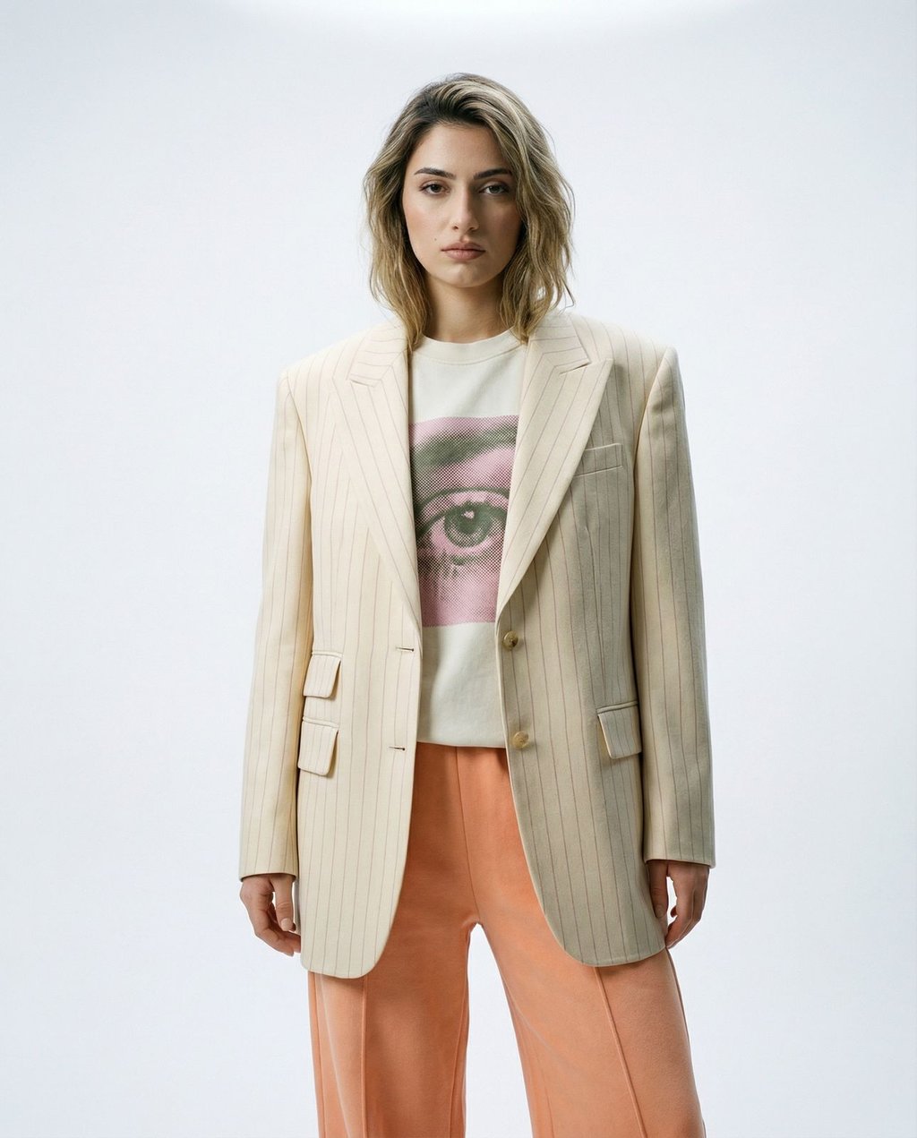 Female model in a cream pinstripe blazer and graphic tee against a neutral off-white backdrop, demonstrating clean consistent AI studio output