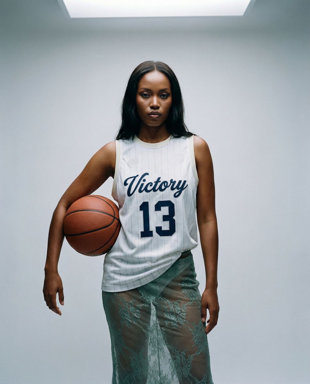 Female model in a white Victory 13 basketball jersey and green lace skirt against a light grey studio backdrop with soft overhead key lighting, illustrating how AI studios encode specific style and lighting presets