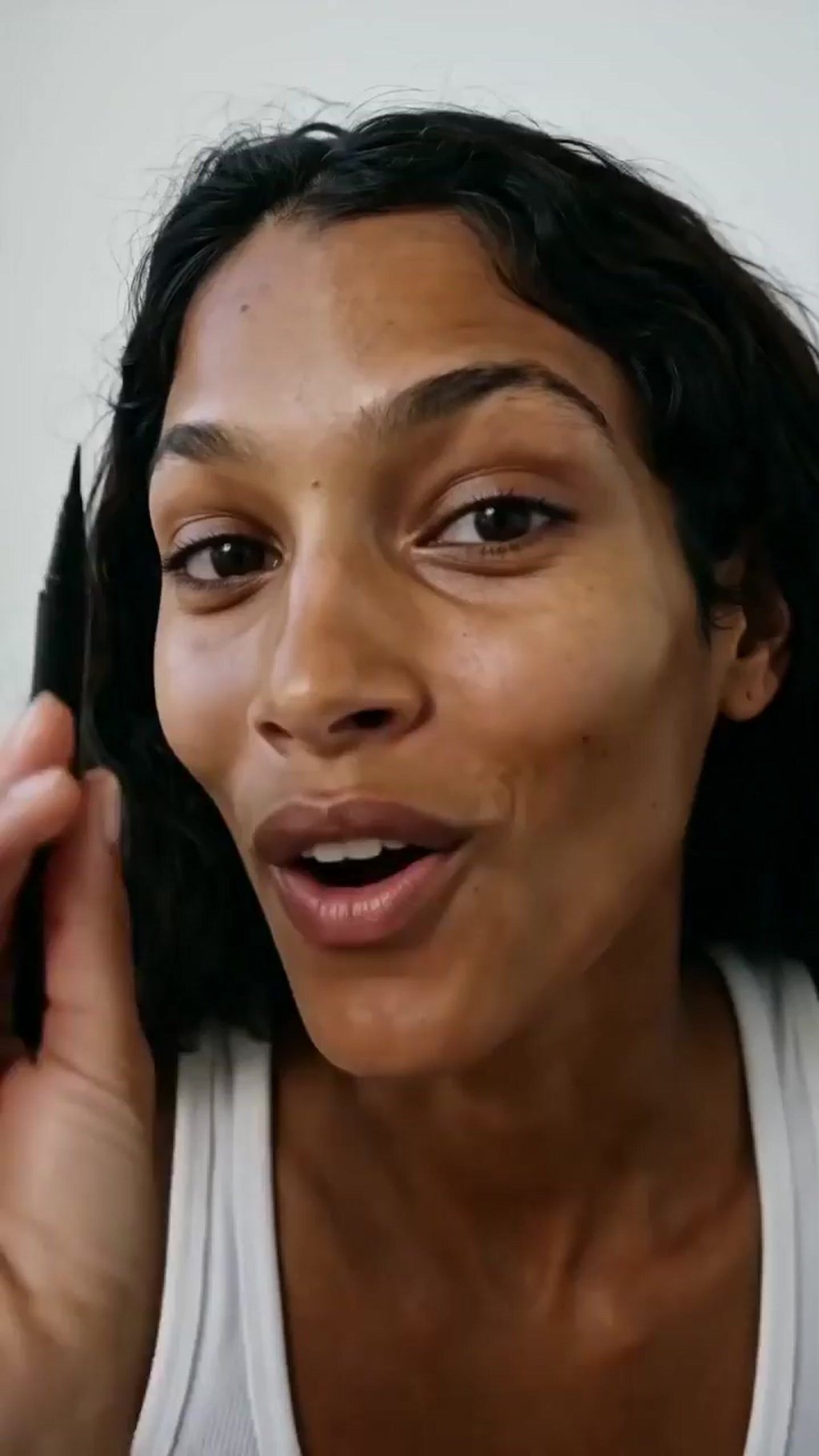 Generated character holding an eyeliner pen up to a phone camera and talking, close selfie framing