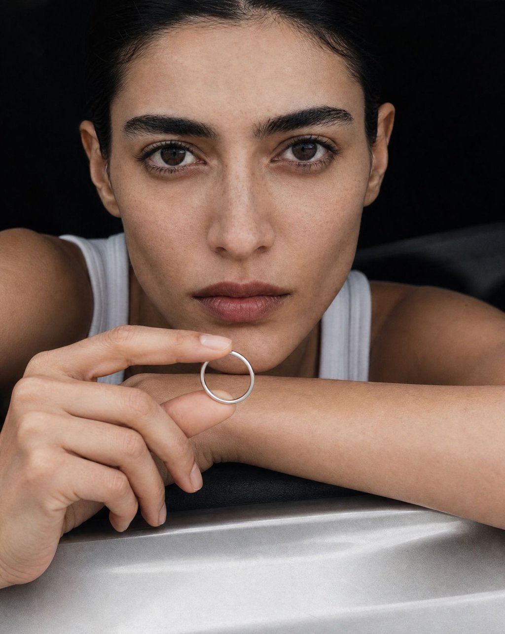 Close-up of woman with olive skin holding a silver ring showing natural color accuracy in a minimalist studio setting