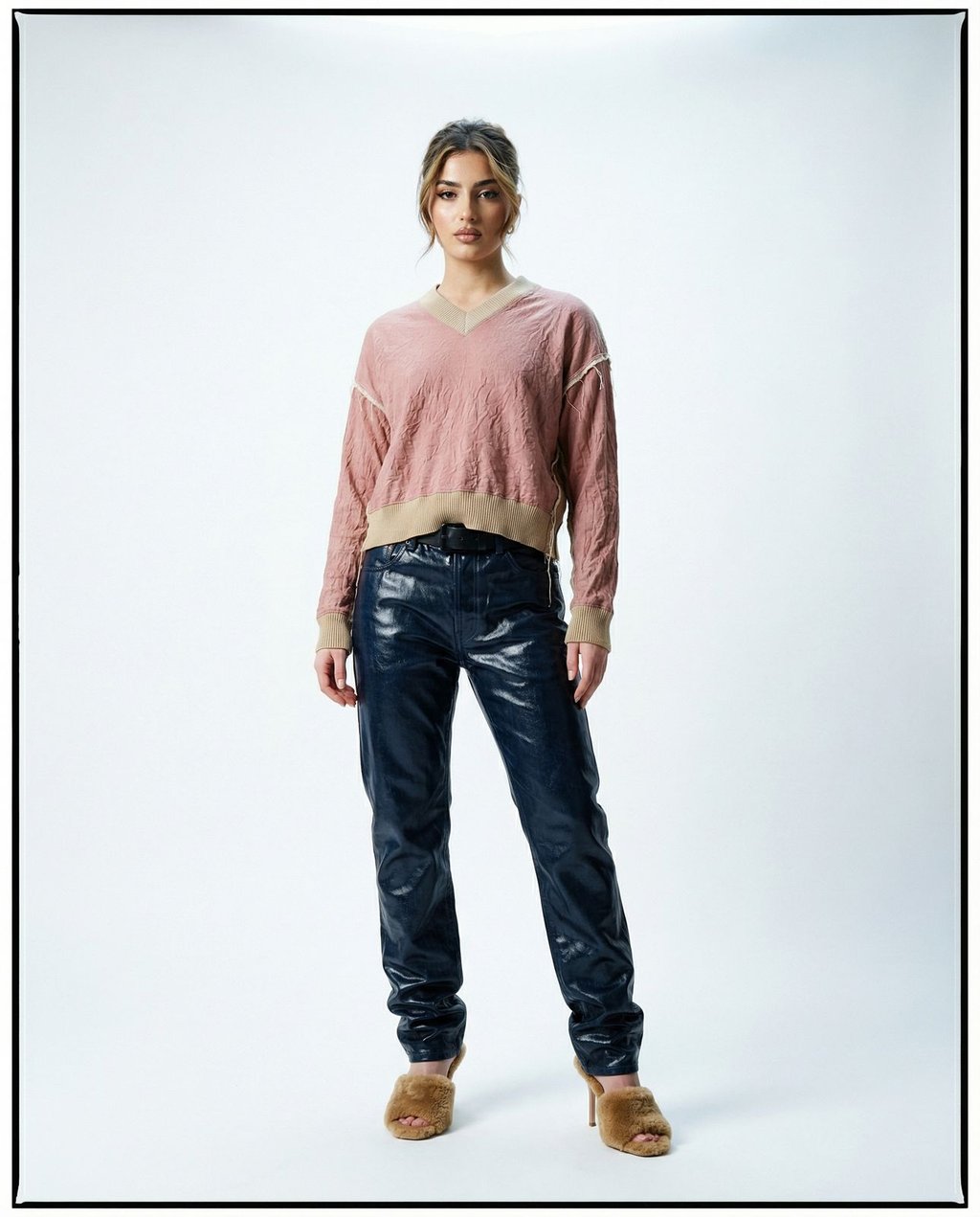 Full-length fashion portrait of a model in a pink sweater and navy leather trousers against a seamless white studio background, showing how studio presets maintain consistent lighting across varied textures