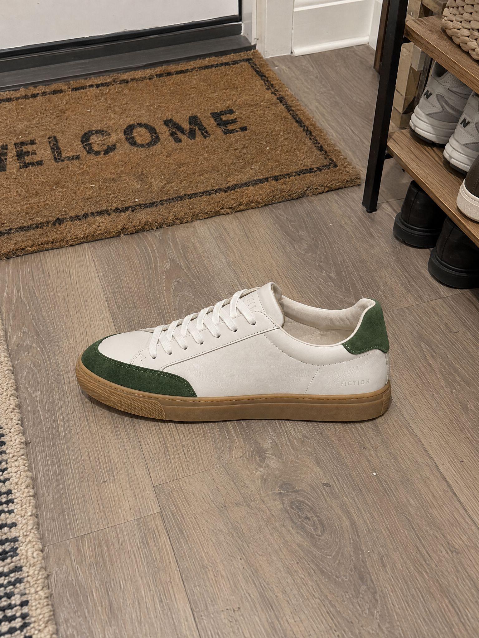White sneaker with green suede panels on a hallway floor next to a doormat and a shoe rack, and the same sneaker in side profile on white - Before