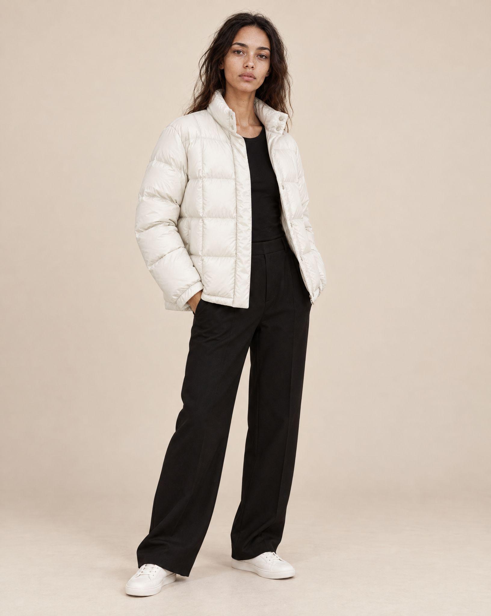 Cream quilted puffer jacket laid flat, and the same jacket worn open over a black top by a woman against a beige backdrop - After