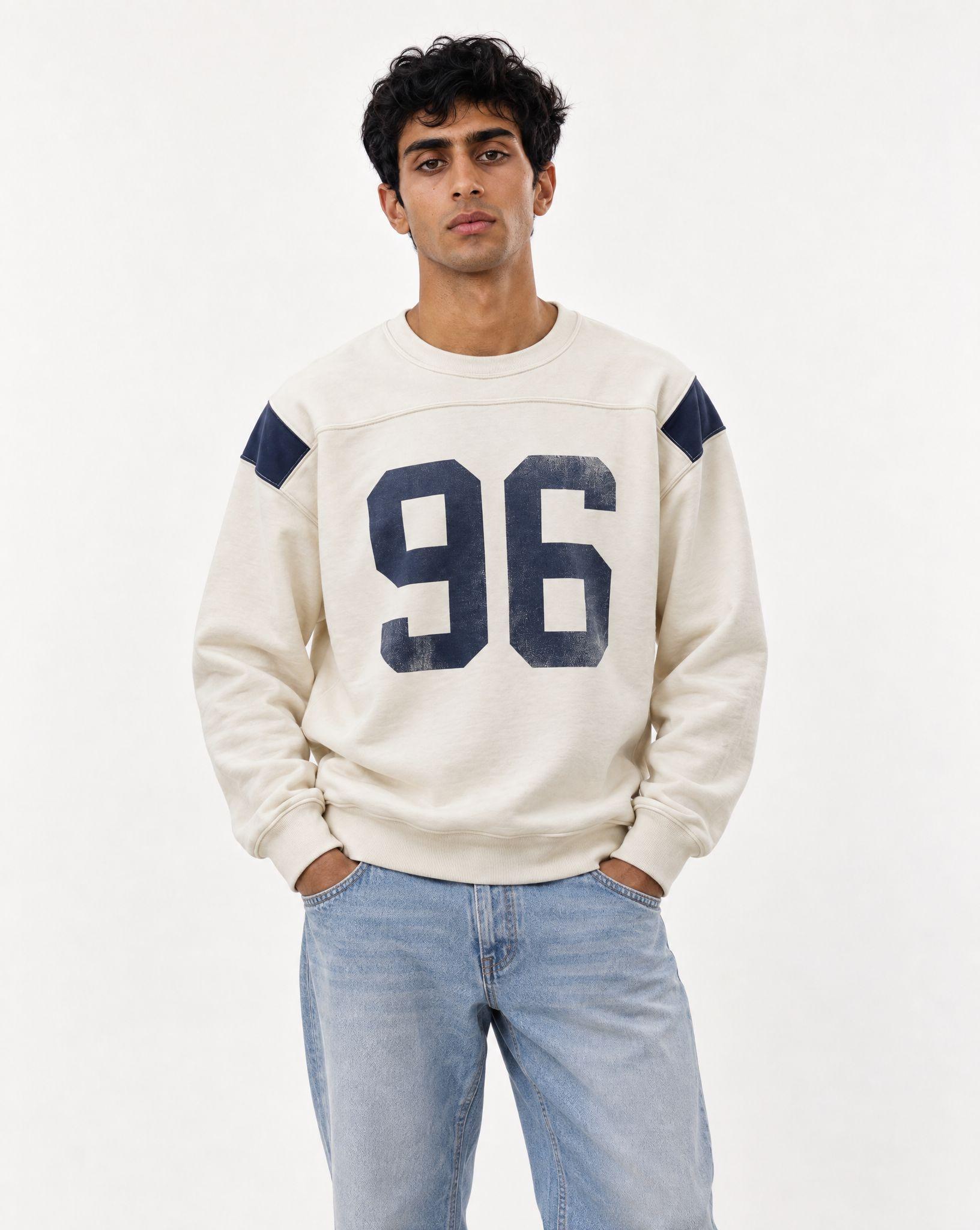 Cream sweatshirt with a navy number 96 laid flat, and the same sweatshirt worn by a young man in light blue jeans - After