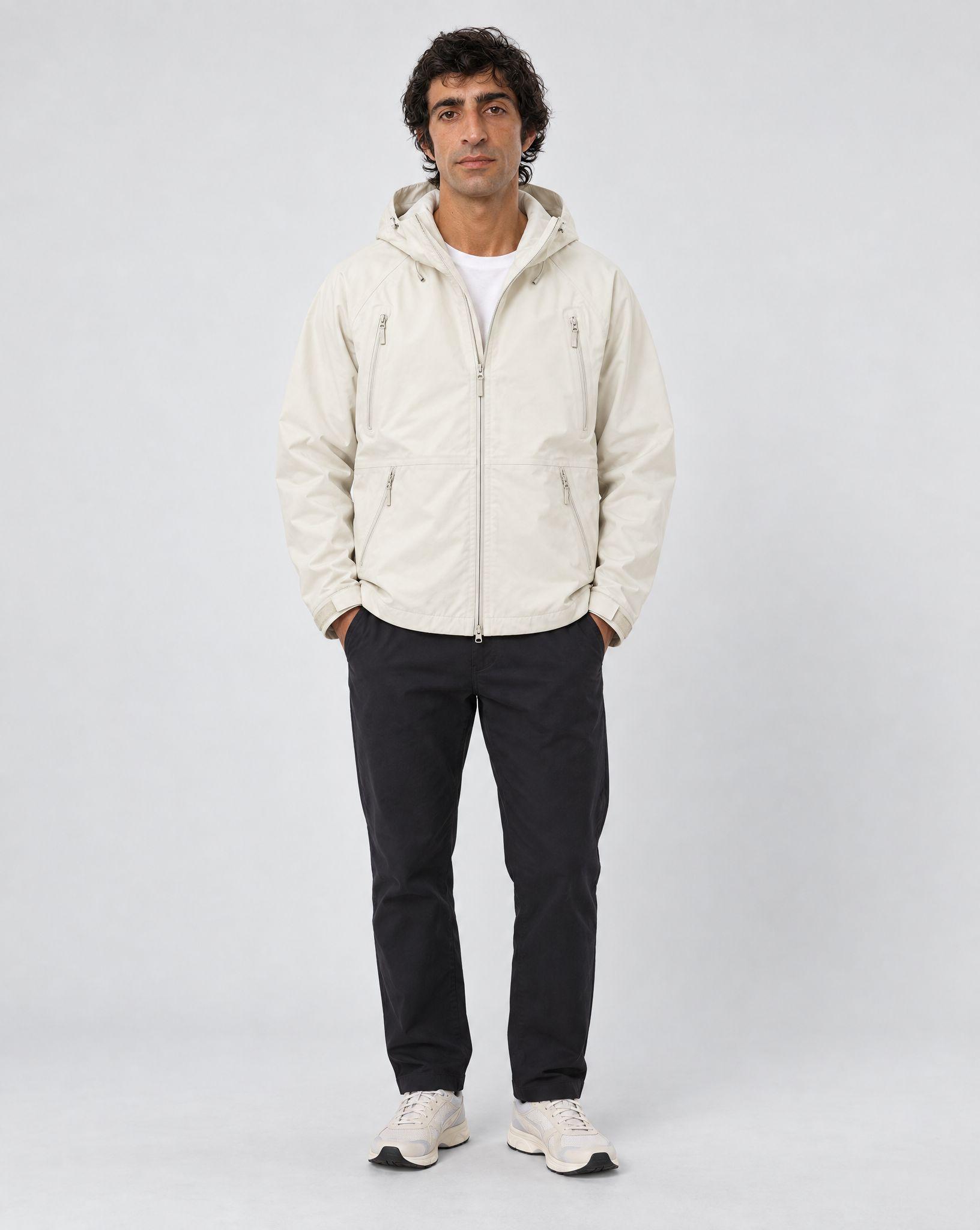 Cream hooded shell jacket laid flat, and the same jacket worn zipped by a man in dark trousers against a light gray backdrop - After