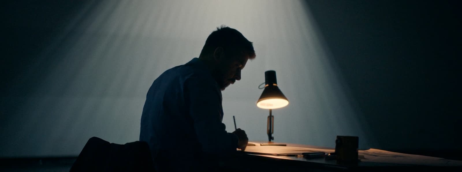 a man sitting in front of a desk with a lamp on it