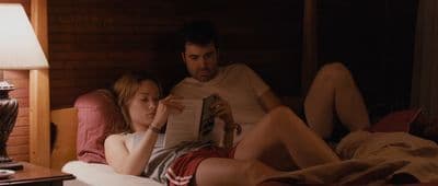 a man and a woman laying in bed reading a book