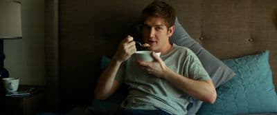 a man laying in bed eating cereal from a bowl