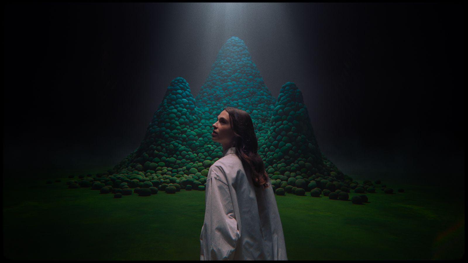 a woman standing in front of a green mountain