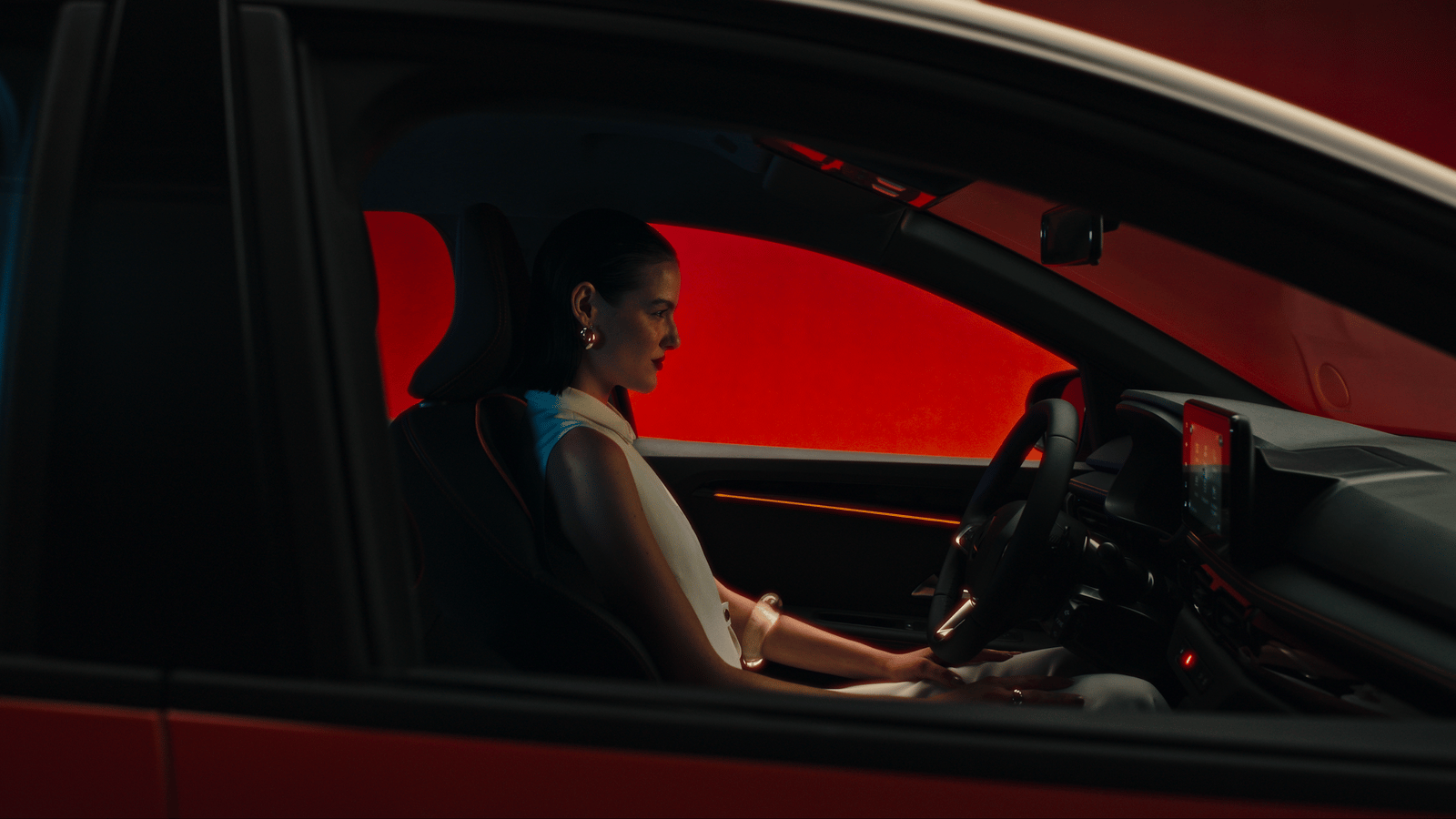a woman sitting in a car with her hand on the steering wheel