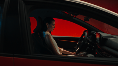 a woman sitting in a car with her hand on the steering wheel