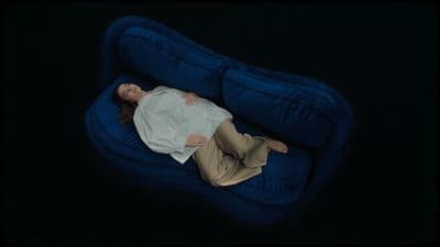 a woman laying on a blue couch in the dark