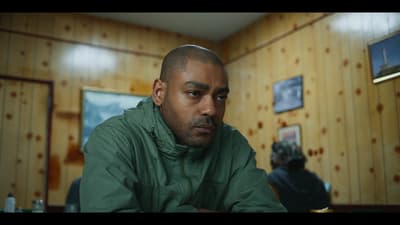 a man in a green jacket sitting in a room