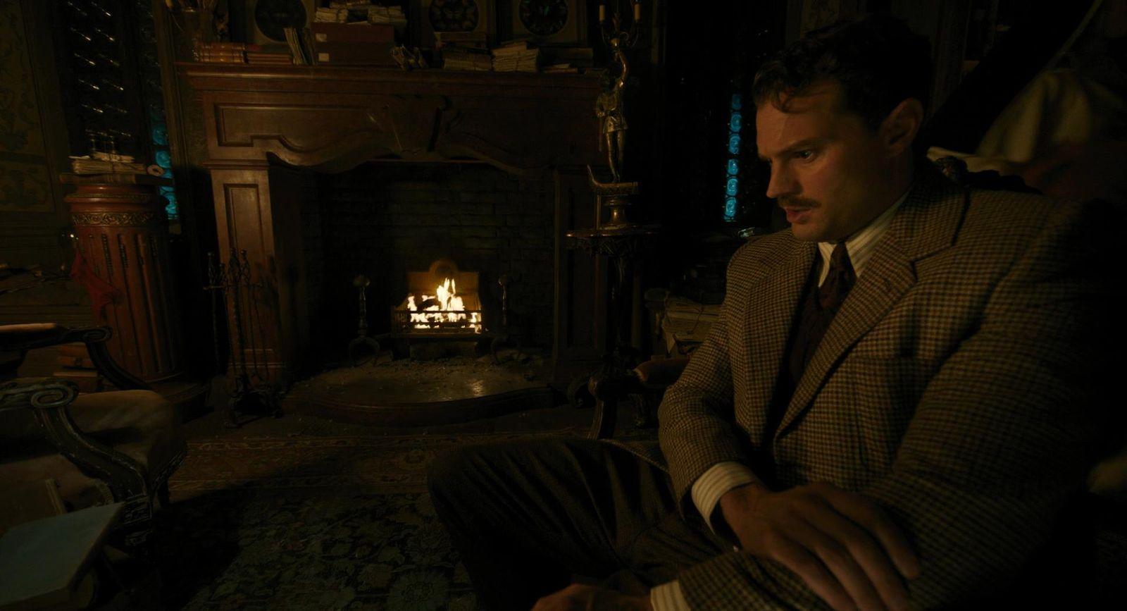a man in a suit sitting in front of a fire place