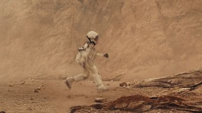 a man in a space suit running in the desert
