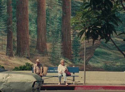a couple of people sitting on a bench next to a forest