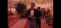 a man in a tuxedo is walking down a hall