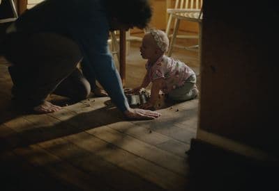 a woman kneeling down next to a baby on the floor