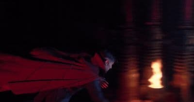 a man in a red cape standing in front of a fire