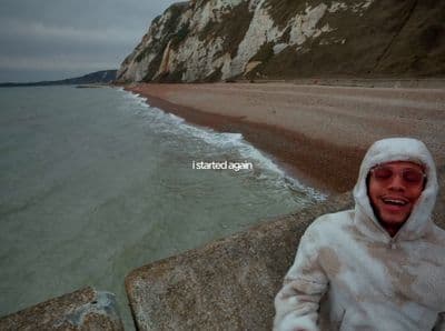 a man in a white jacket standing on a beach next to the ocean