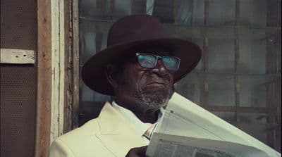 a man in a hat and glasses reading a newspaper