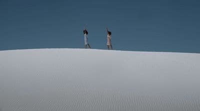 two people standing on top of a white sand dune
