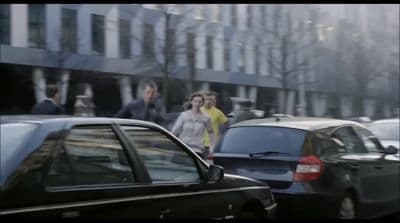 a group of people walking down a street next to parked cars