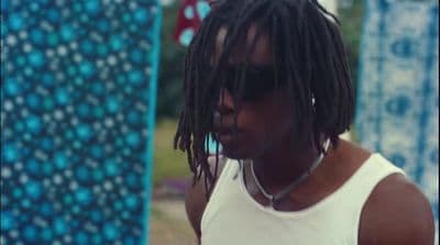 a man with dreadlocks standing next to a surfboard