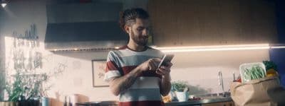 a man standing in a kitchen looking at a cell phone