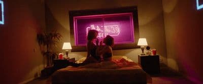 two women sitting on a bed in front of a window