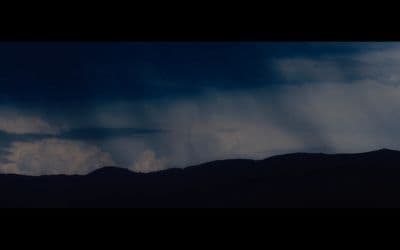 a dark sky with clouds and mountains in the background