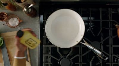 a person holding a bottle of mustard near a pan on a stove