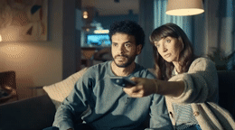 a man and a woman sitting on a couch holding remotes