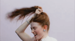a woman with red hair is smiling and touching her hair