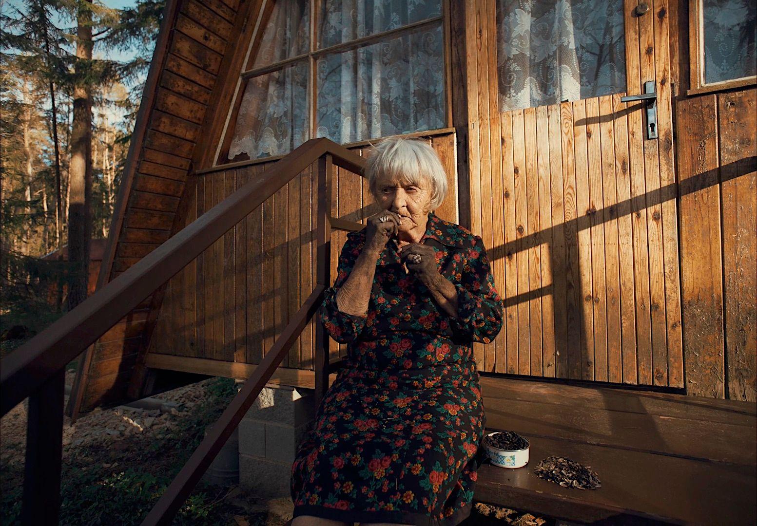 an older woman sitting on a porch next to a wooden building