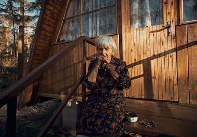 an older woman sitting on a porch next to a wooden building
