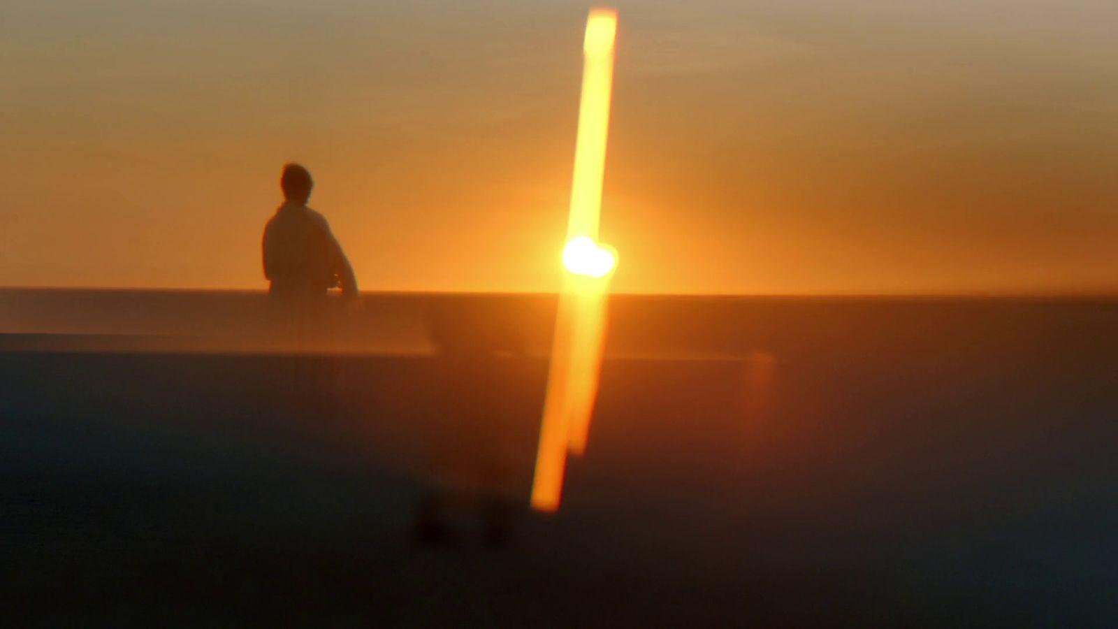 a man sitting on a bench watching the sun go down