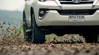 the front of a white car with leaves on the ground